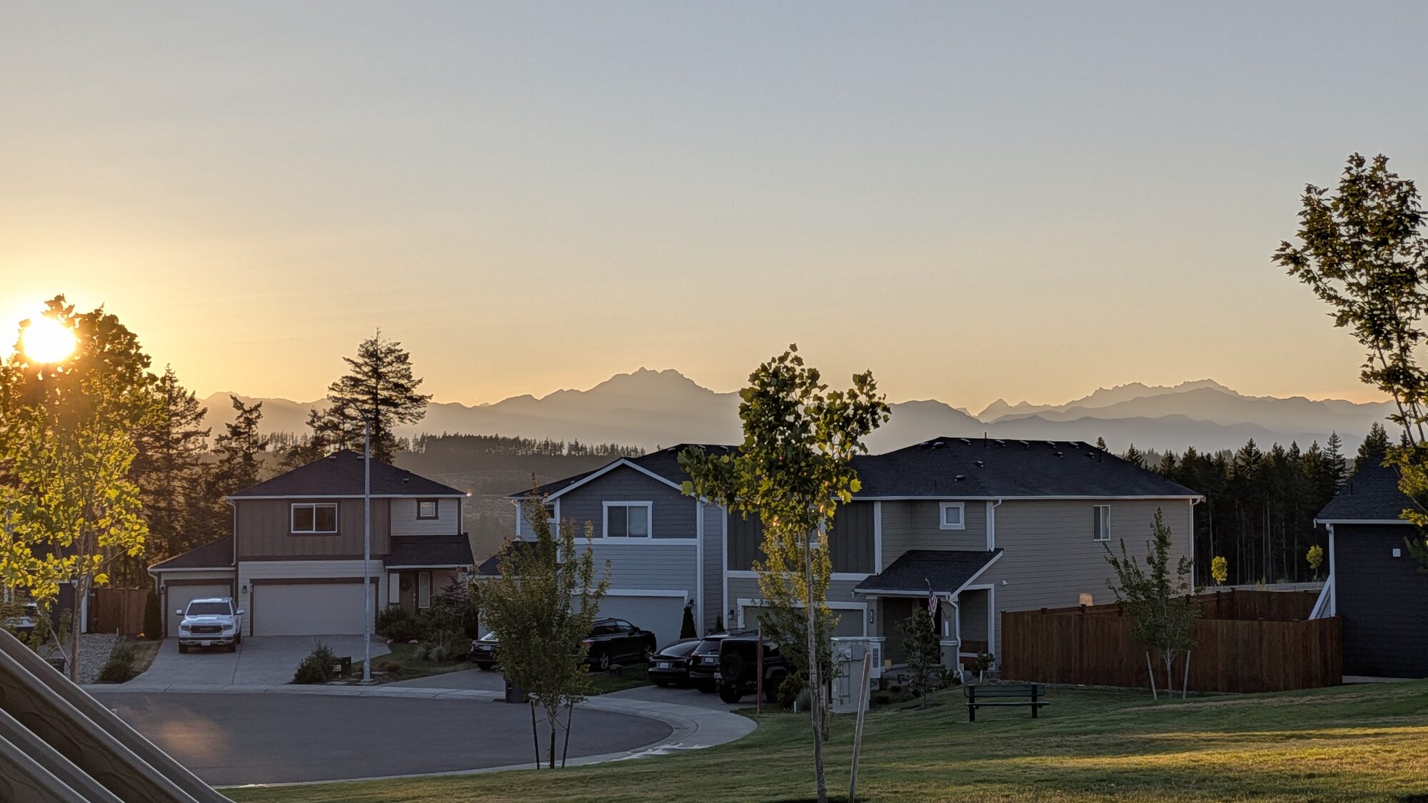An Olympic Ridge cul-de-sac and lawn at sunrise, with parked cars and the Olympic Mountains beyond