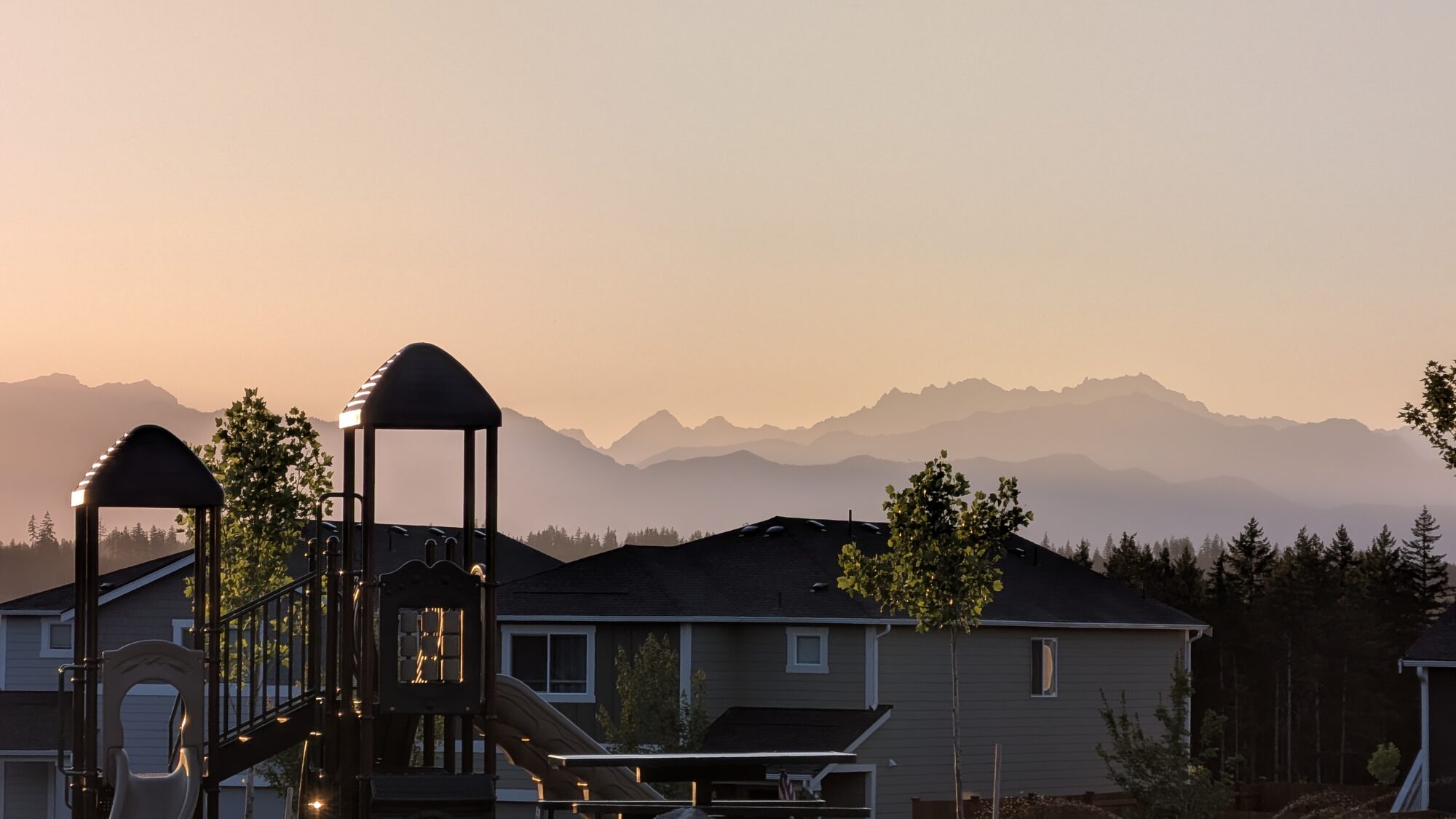The Olympic Ridge community park playground at golden hour with layered Olympic Mountain ridgelines behind